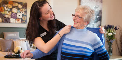A seasons staff member helping a resident put a sweater on